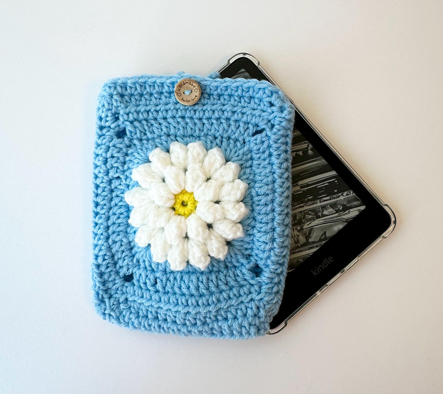 blue granny square crocheted kindle paperwhite sleeve featuring a raised white flower and wood button closure