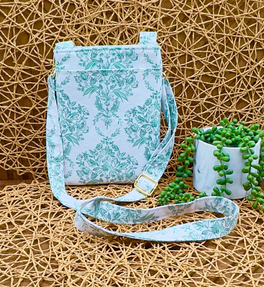 Floral-patterned crossbody bag on a textured surface with a plant in the background