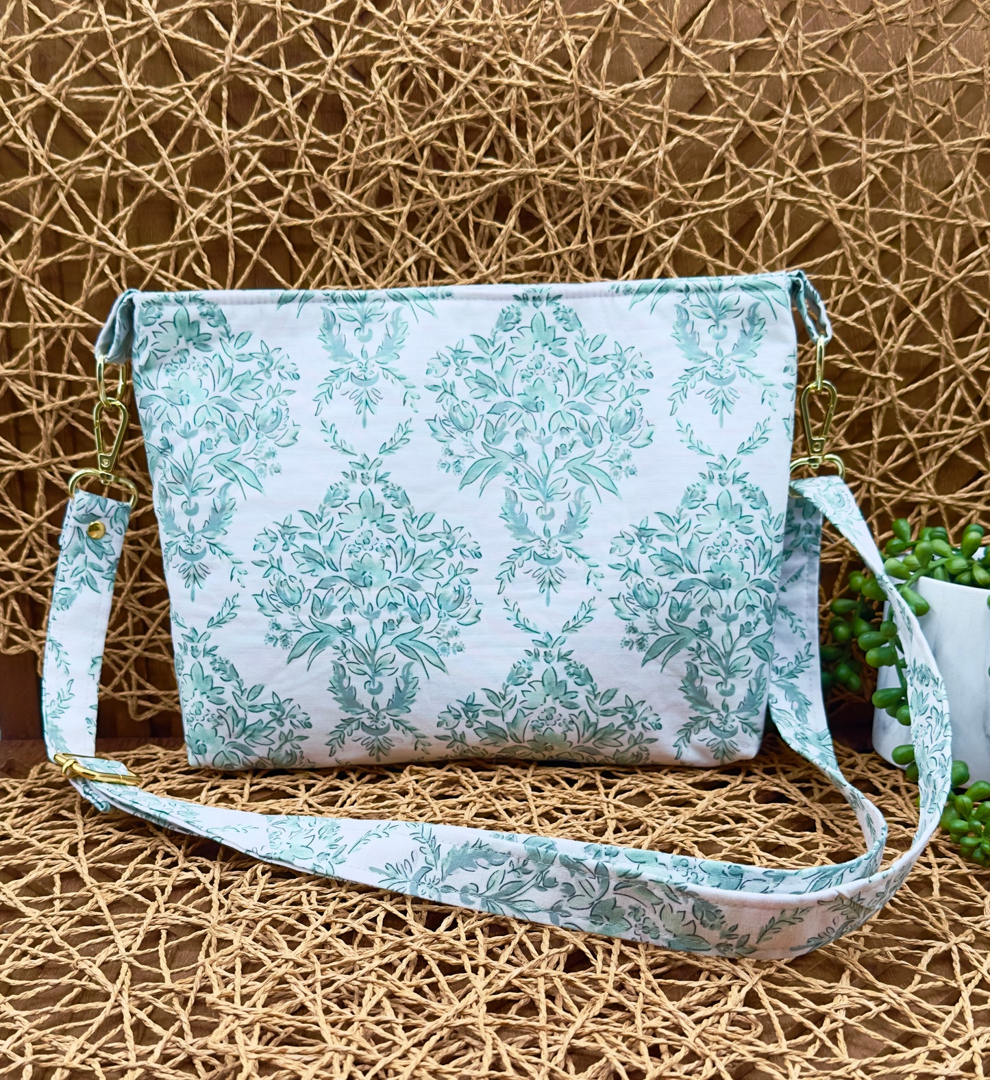 green floral cotton crossbody bag next to plant