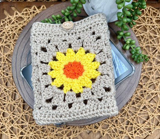 beige granny square crocheted kindle paperwhite sleeve featuring a yellow flower and wood button closure