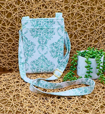 Floral-patterned crossbody bag on a textured surface with a plant in the background